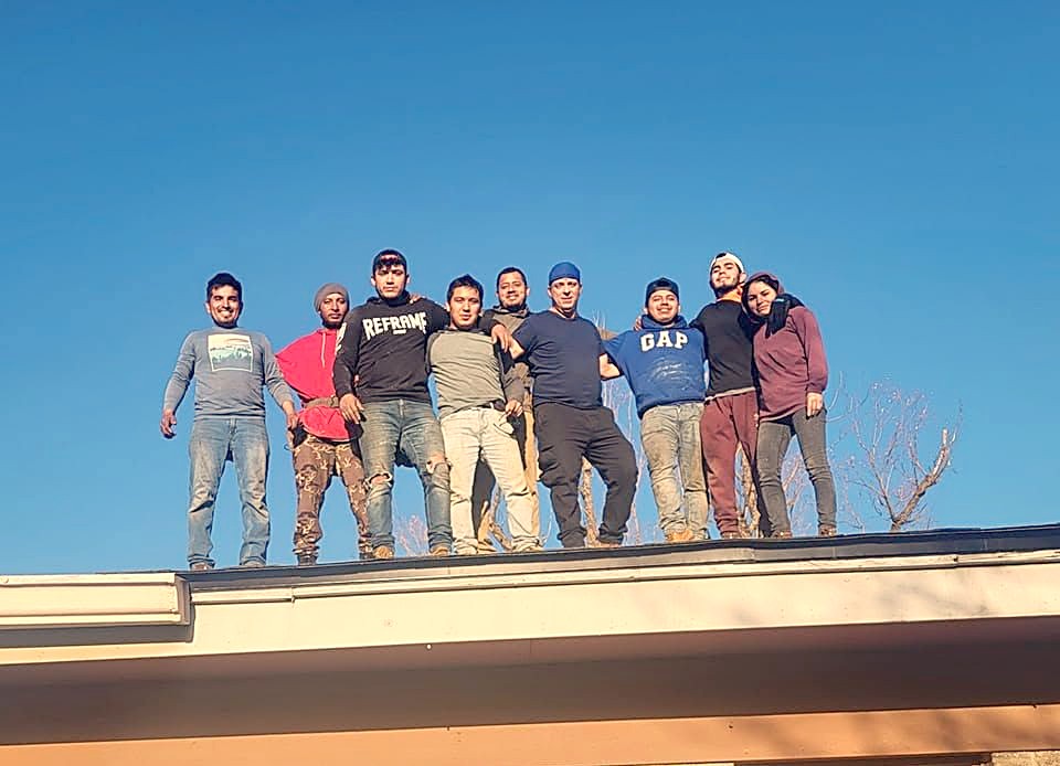 A roofing crew standing along the ridge of a house against a clear blue sky