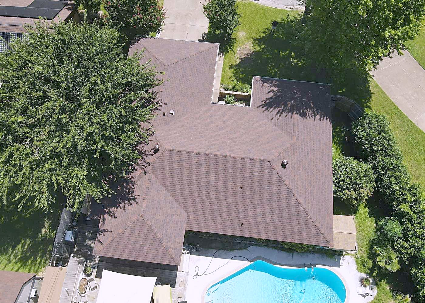 Aerial view of a finished brown shingle roof on a home with a swimming pool in the yard