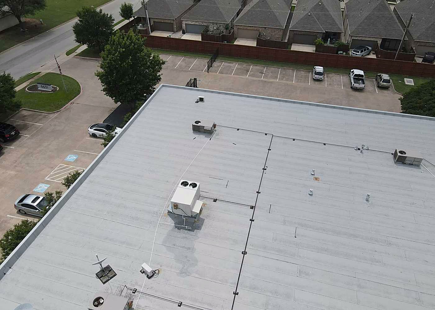 A white flat roof on a commercial building, with rooftop units and a parking lot below
