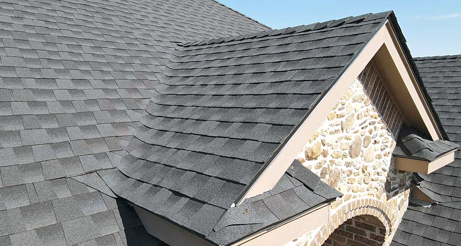 Finished charcoal architectural shingles on a hip roof beside a stone gable end