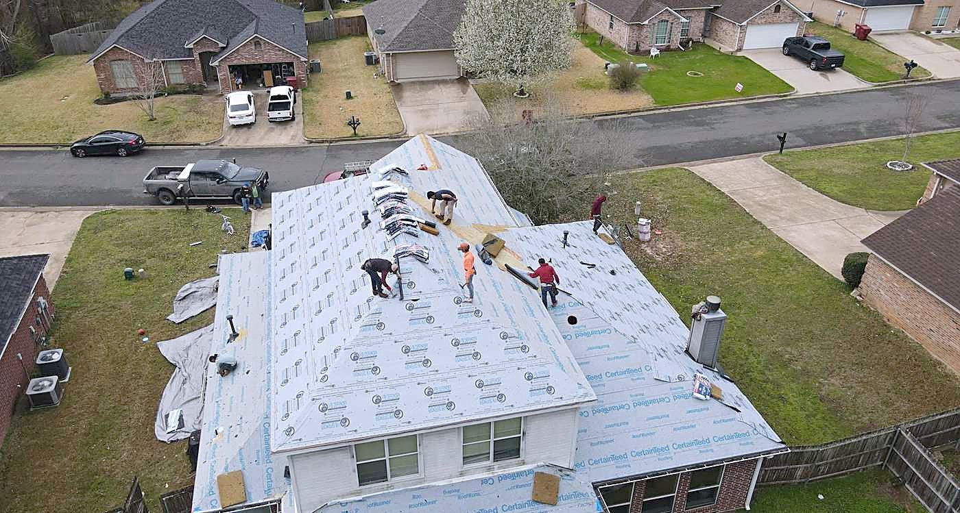 Aerial view of a crew installing shingles over synthetic underlayment on a single-story home