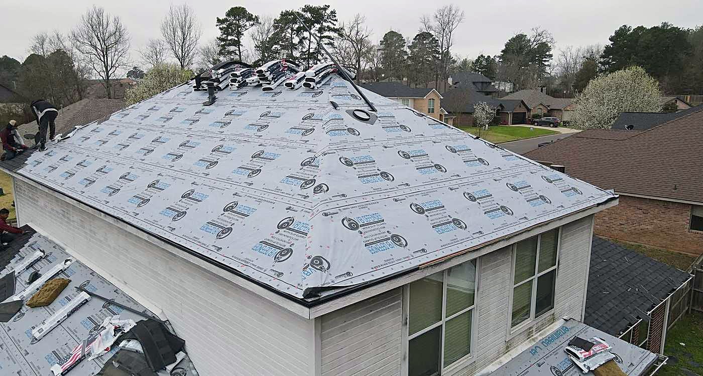 A hip roof decked and papered with grey synthetic underlayment, ready for shingles